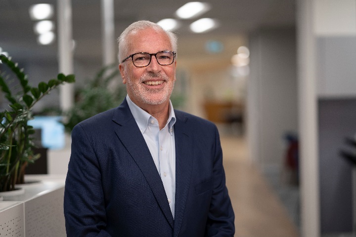 TelstraSuper CEO Chris Davies faces the camera smiling. He's wearing a dark blue suit, glasses and is in the TelstraSuper office.